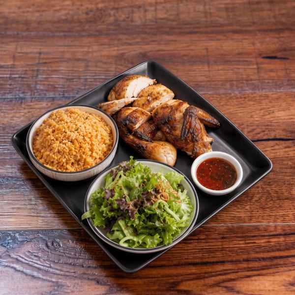 Grilled chicken pieces, rice, green salad, and chili sauce on a black plate.