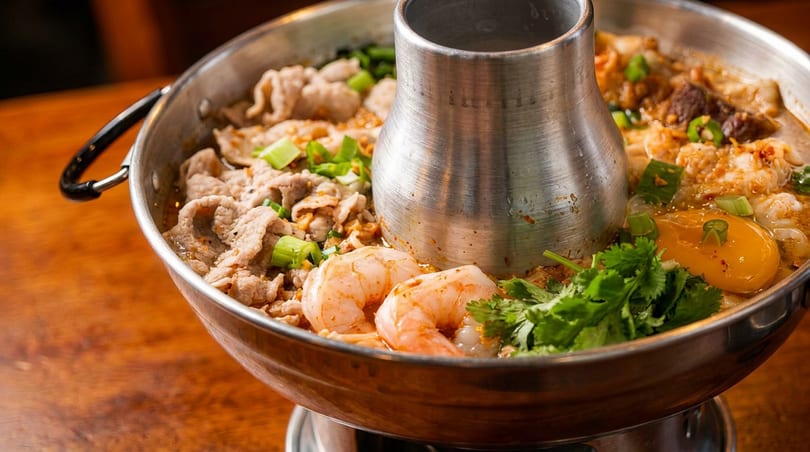 A hot pot with shrimp, sliced pork, egg yolk, and green onions in a savory broth.