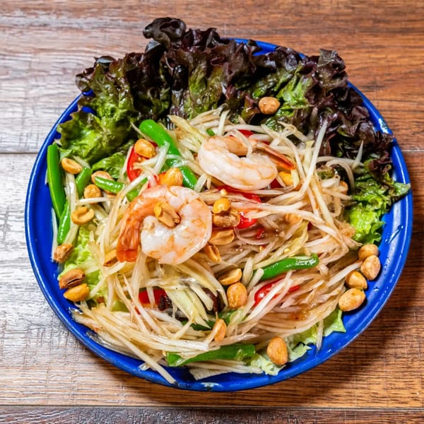 Thai papaya salad with shrimp, peanuts, green beans, and lettuce on a blue plate.