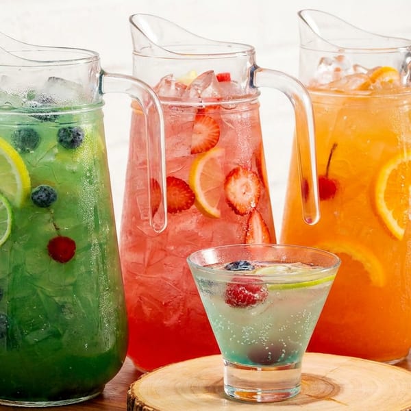Three pitchers of colorful fruit-infused drinks and one glass on a wooden surface.
