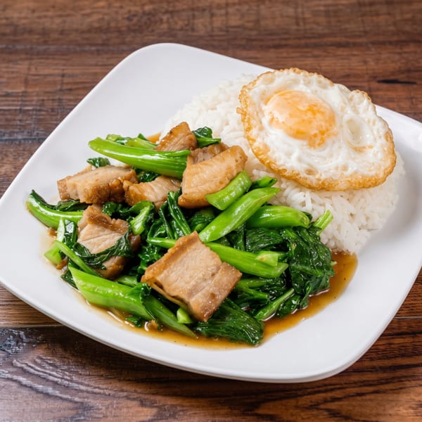 White rice with fried egg, stir-fried Chinese broccoli, and crispy pork belly on a white plate.