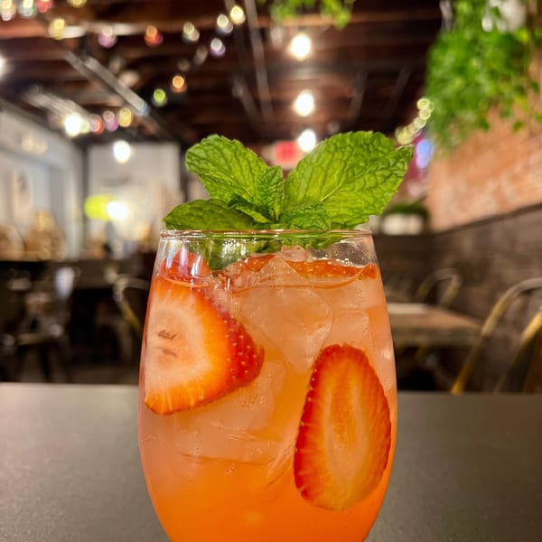 Strawberry cocktail with mint garnish in a restaurant with string lights and hanging plants.