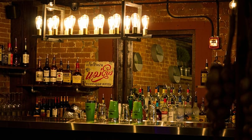 A dimly lit bar with brick walls, shelves of liquor bottles, and a hanging light fixture.