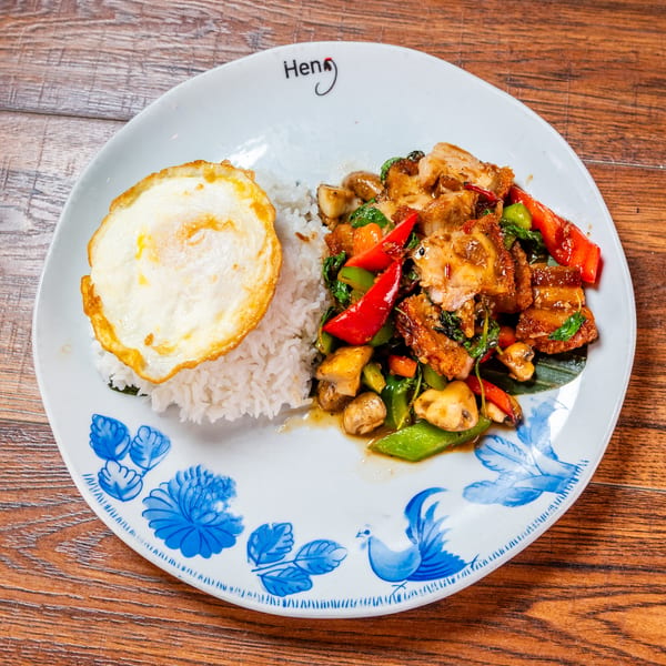 Crispy pork belly stir-fry with rice and a fried egg on a decorative plate.
