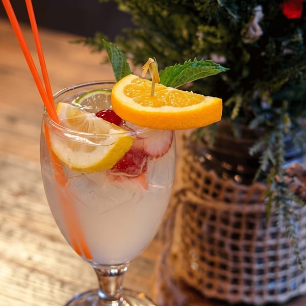 Refreshing drink with lemon, orange, strawberries, and mint on a wooden table next to a plant.